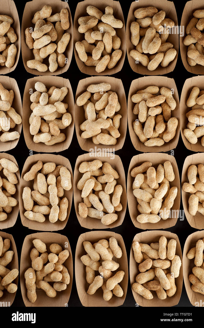 Peanuts with shell in disposable cardboard boxes on a black table. Stock Photo