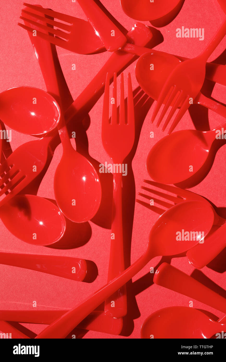 Red disposable plastic cutlery on a red table. Stock Photo
