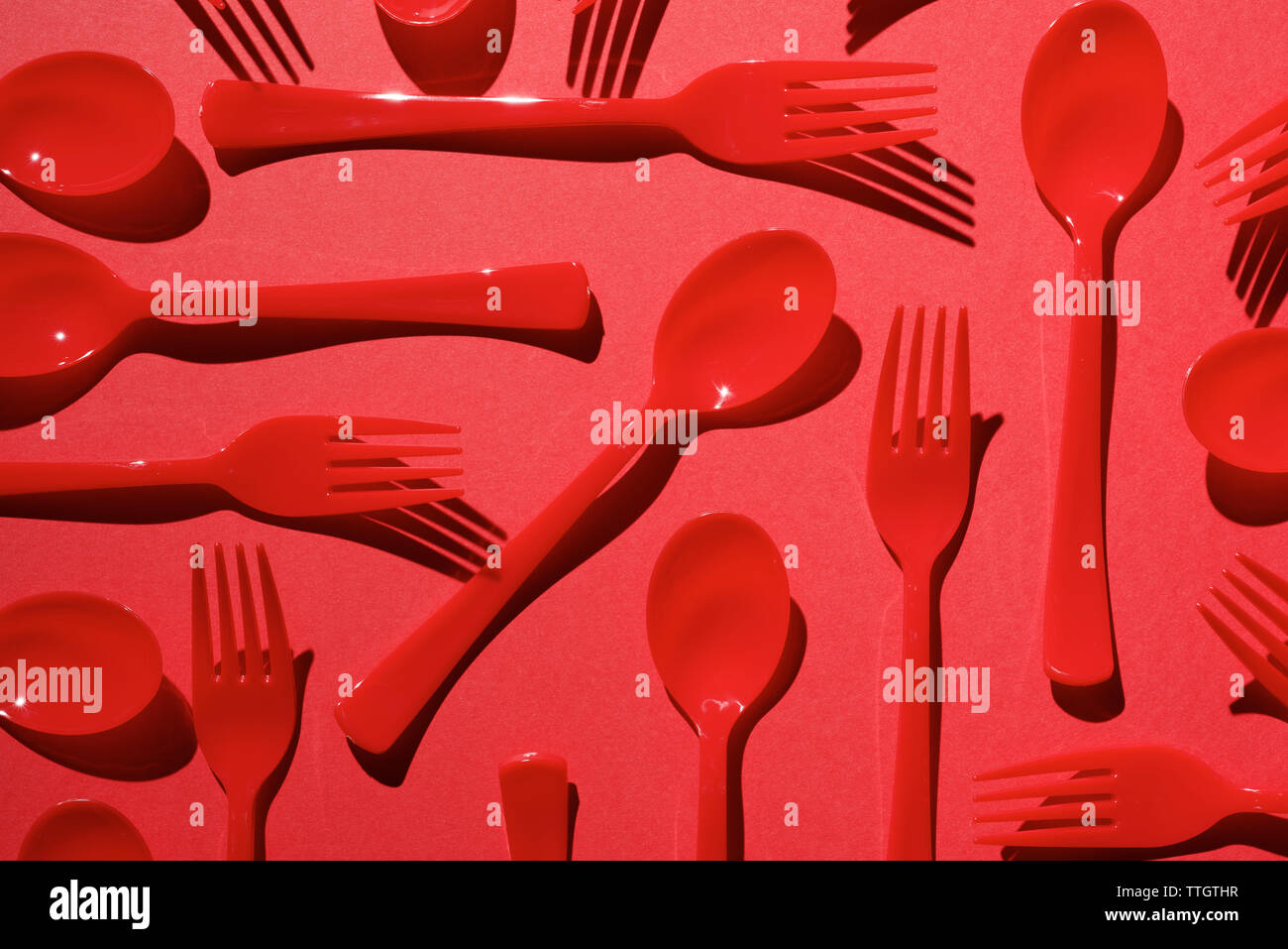 Red disposable plastic cutlery on a red table. Stock Photo