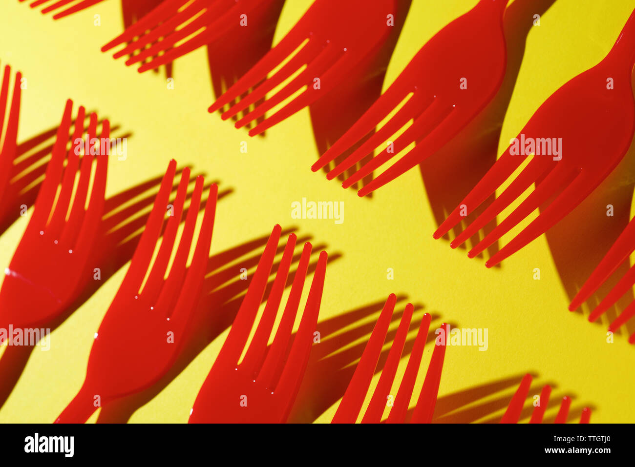 Red disposable plastic cutlery on a yellow table. Stock Photo
