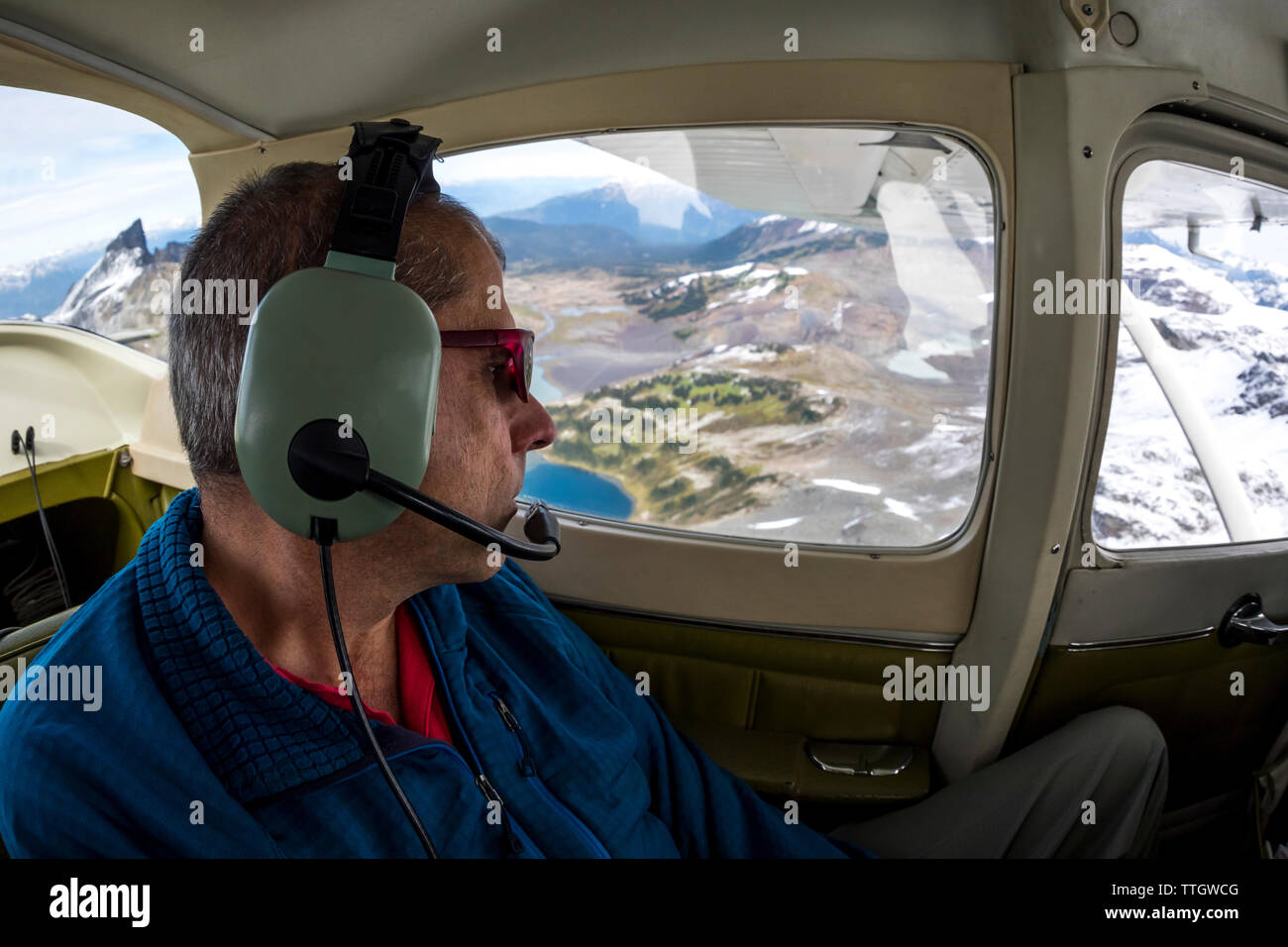 A senior man looks out the window of an airplane at Black Tusk. Stock Photo