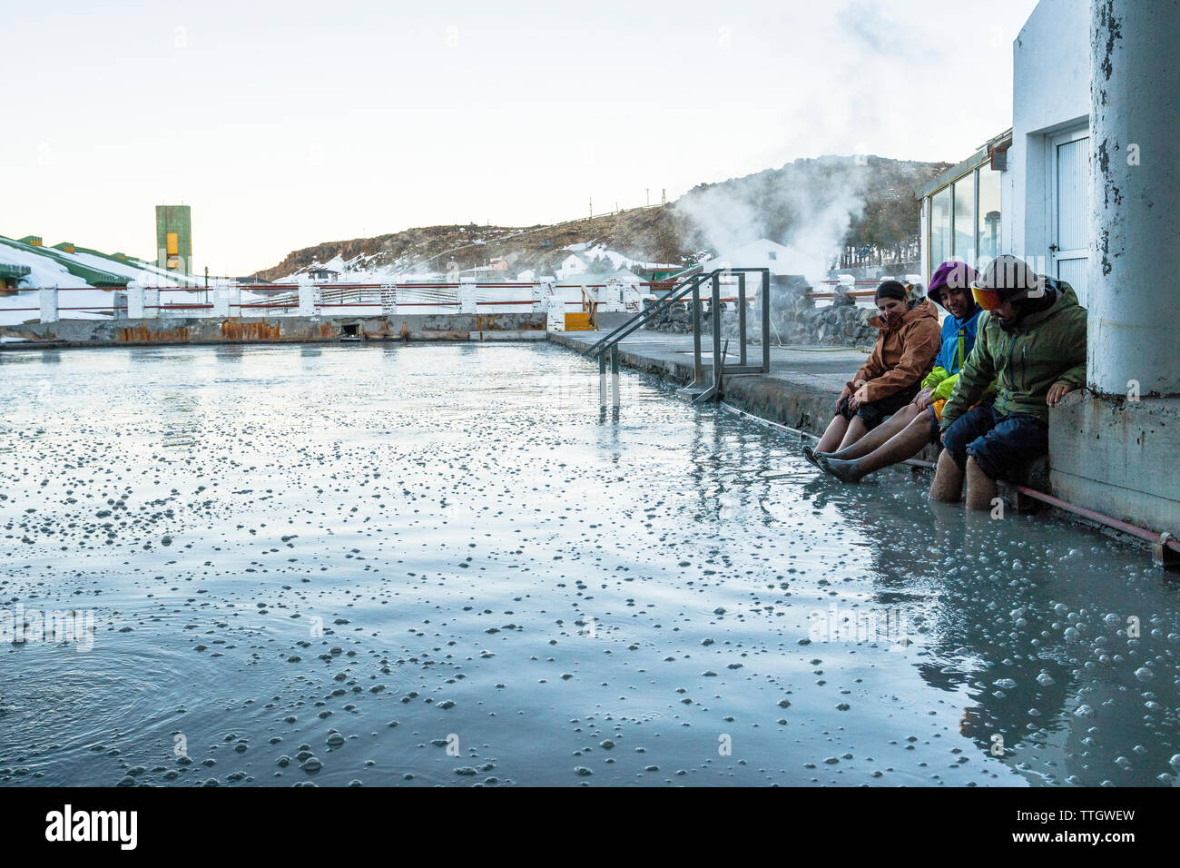 Three people soak their feet in a mud bath after a day of snowboarding Stock Photo