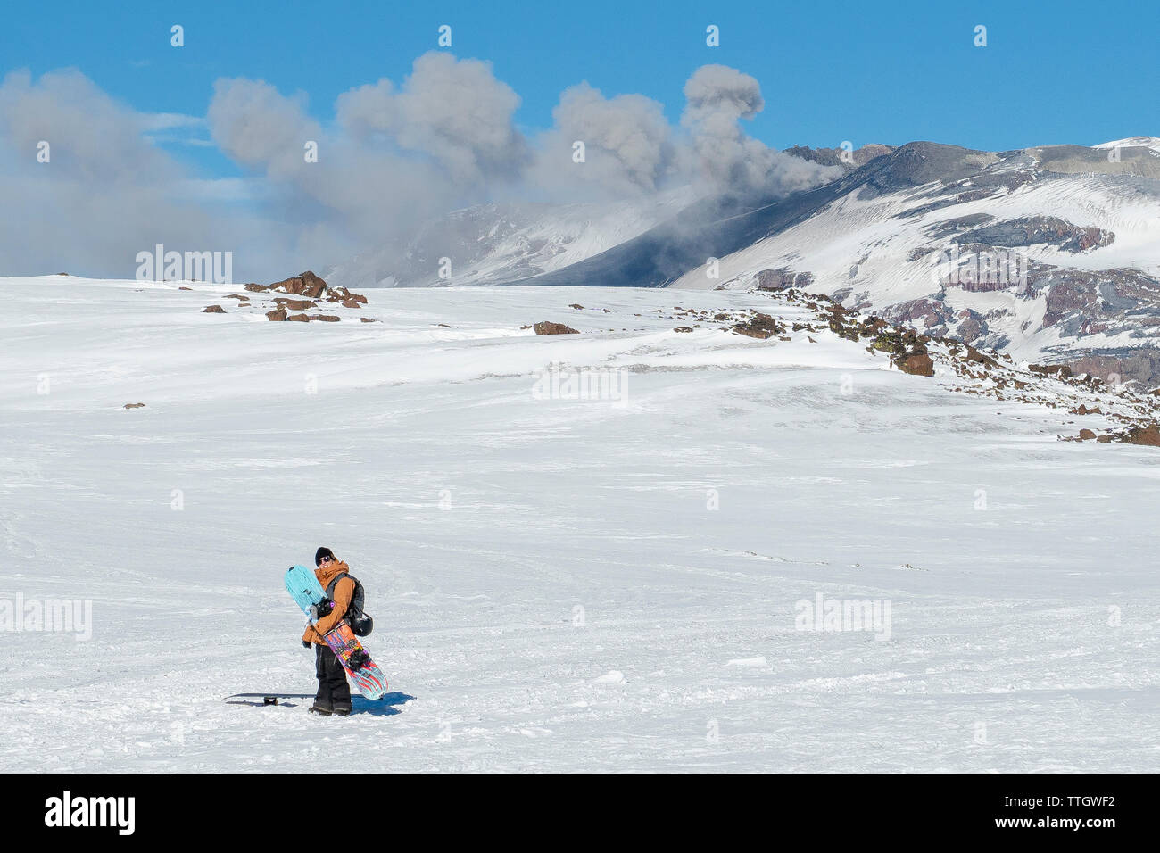 A women stands with her splitboard, as Volcan Copahue spews ash behind Stock Photo