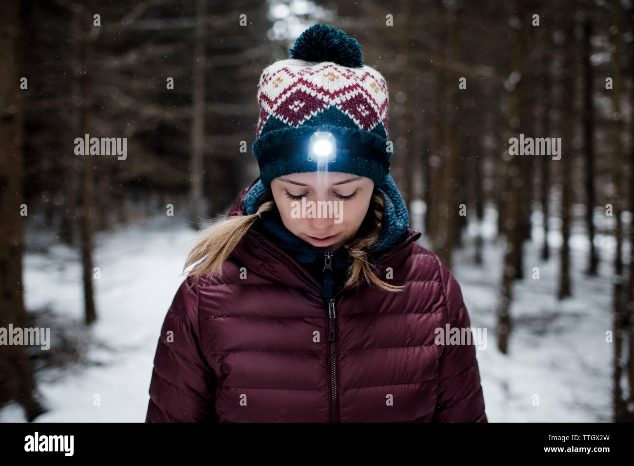 woman looking down in the forest with head torch on whilst snowing Stock Photo