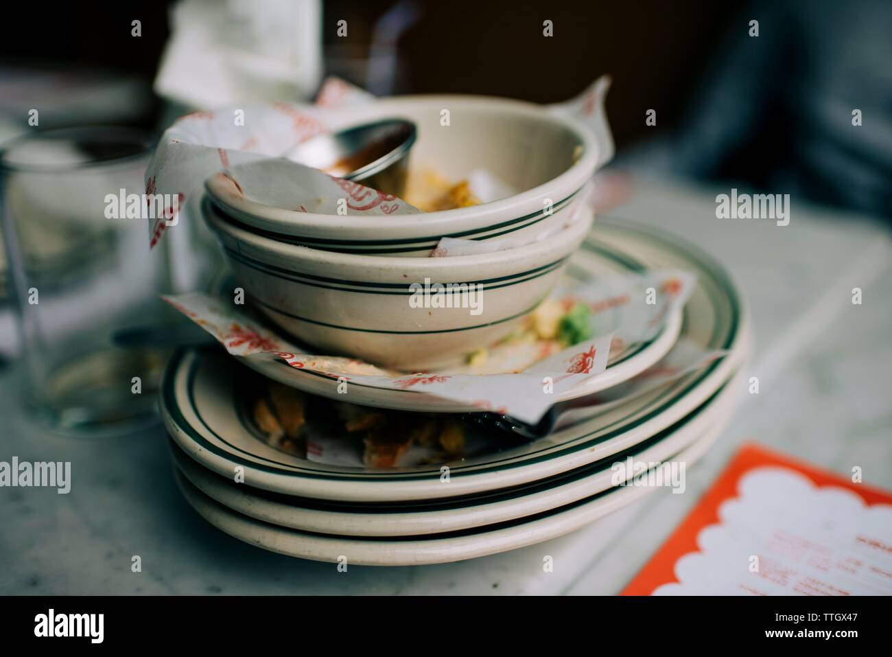 dirty dishes stacked up on a restaurant table with leftover food Stock Photo