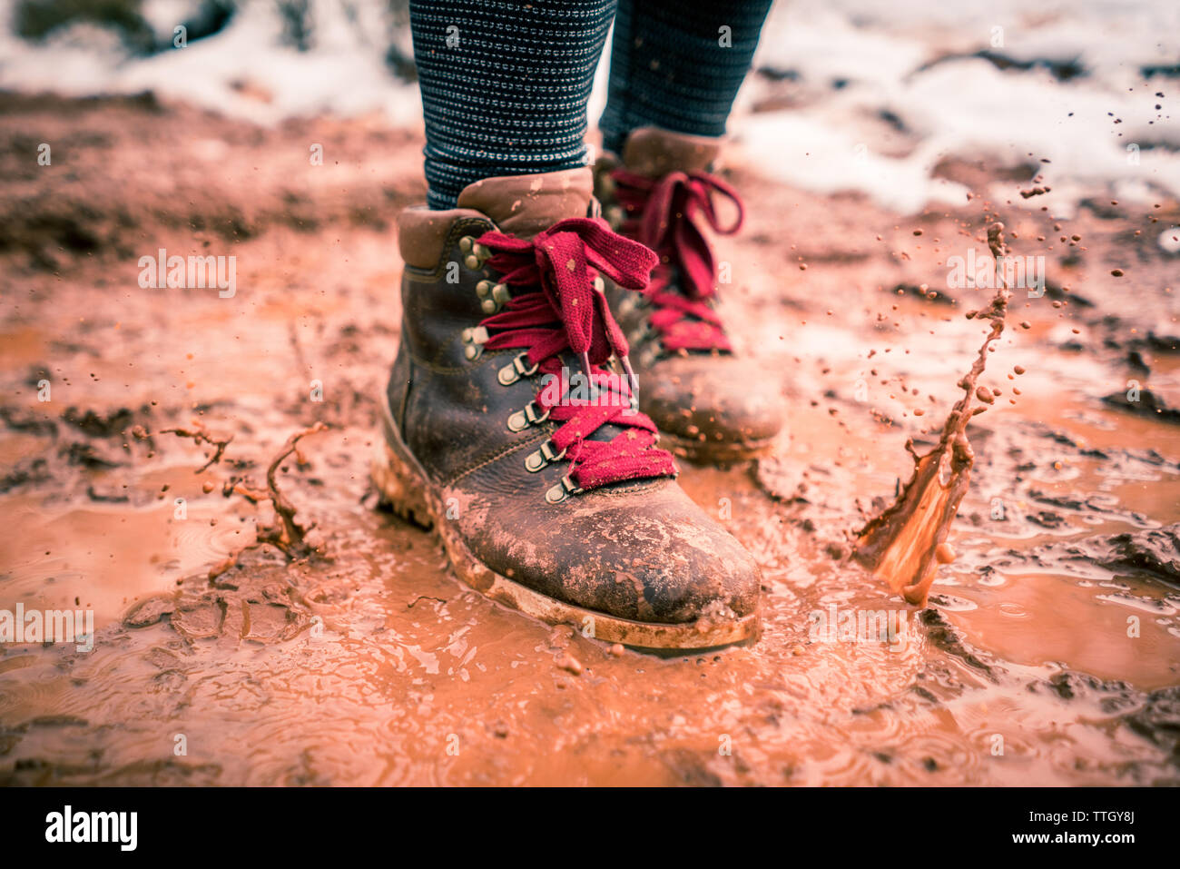 Stylish Hiking Boot Splashing on Trail in Red Mud Stock Photo