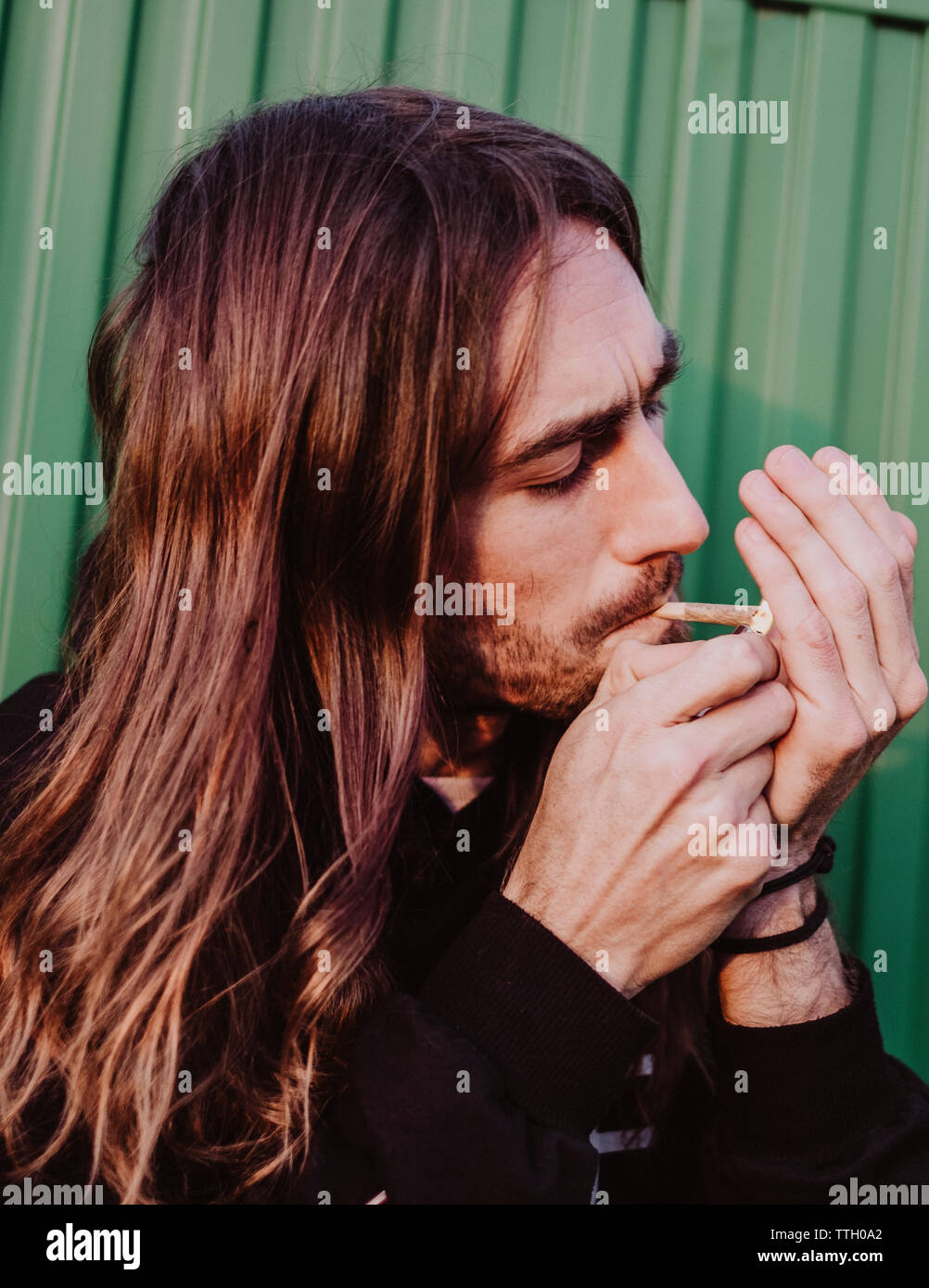 A man lighting a cigarette in a green background with a warm light Stock Photo