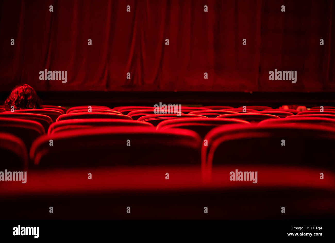 A woman with red hair sitting on a velvet red seat at an empty theater Stock Photo
