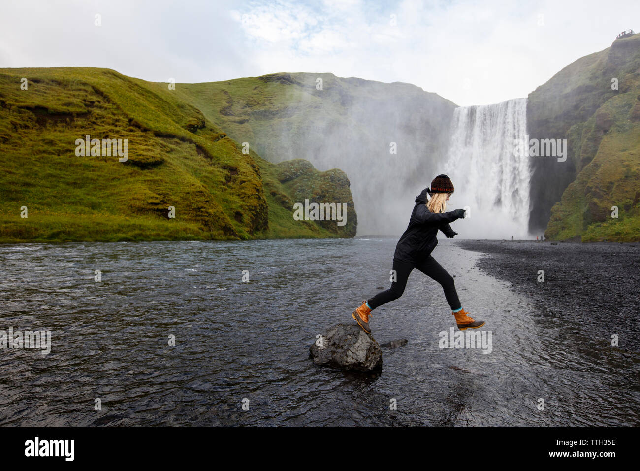 A millenial woman jumps from a rock near Skogafoss, Iceland. Stock Photo
