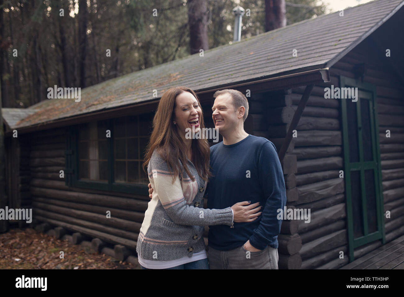 A Married Couple Laughs in Front of a Cabin Stock Photo