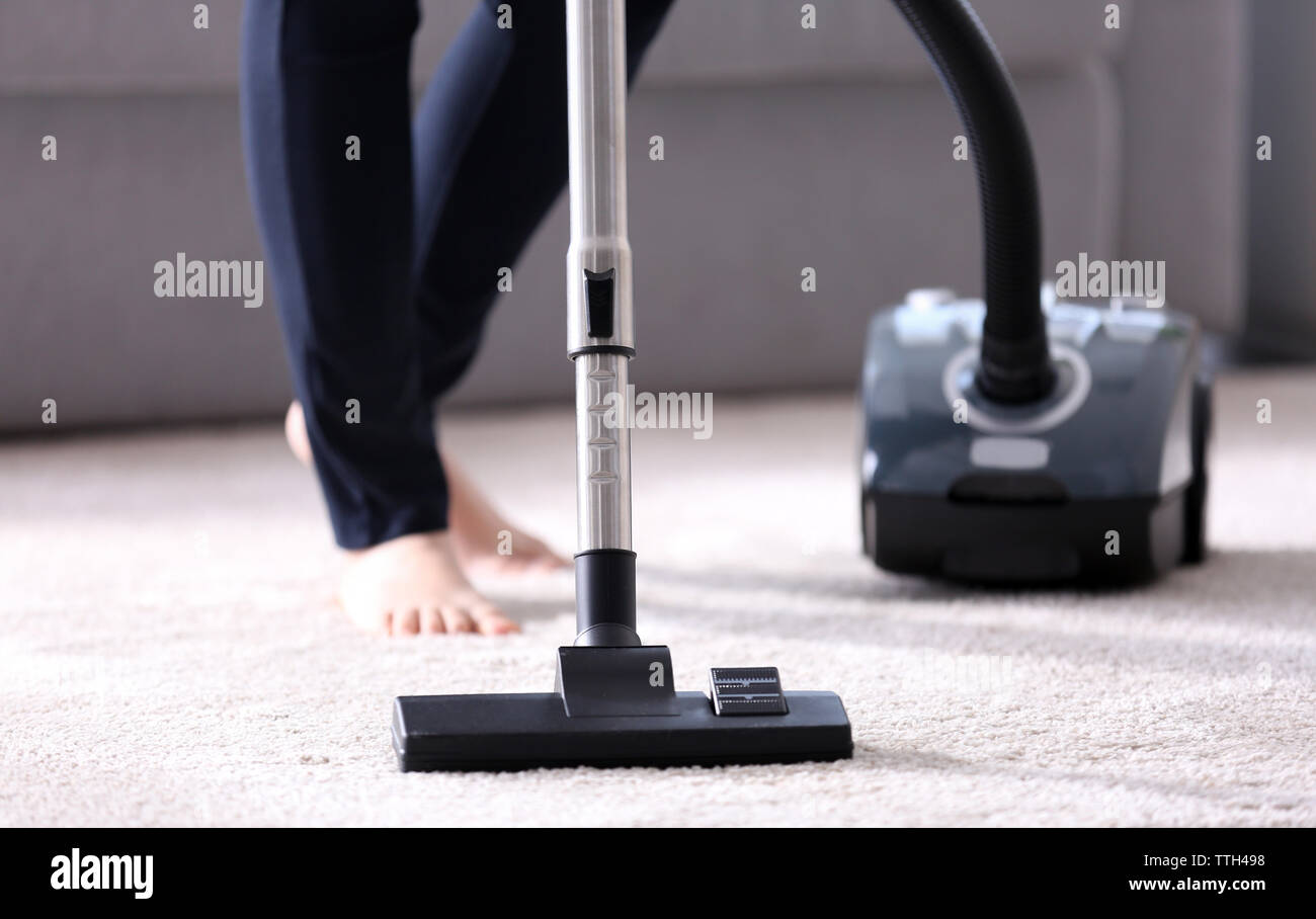 Woman using vacuum cleaner on carpet at home in the living room, close ...