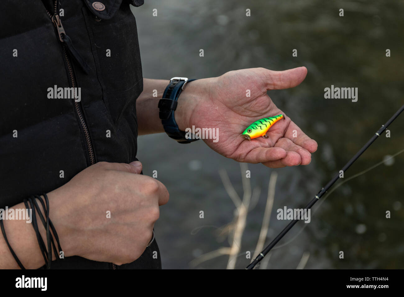 Fisherman next to a small river holding a colourful bait in his hand Stock Photo