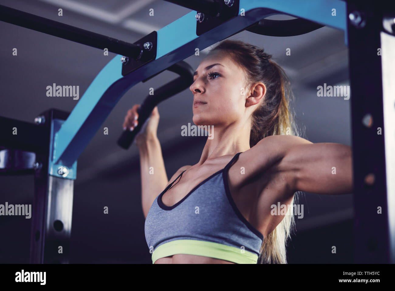 Front profile of young woman doing chin ups at fitness centre Stock Photo