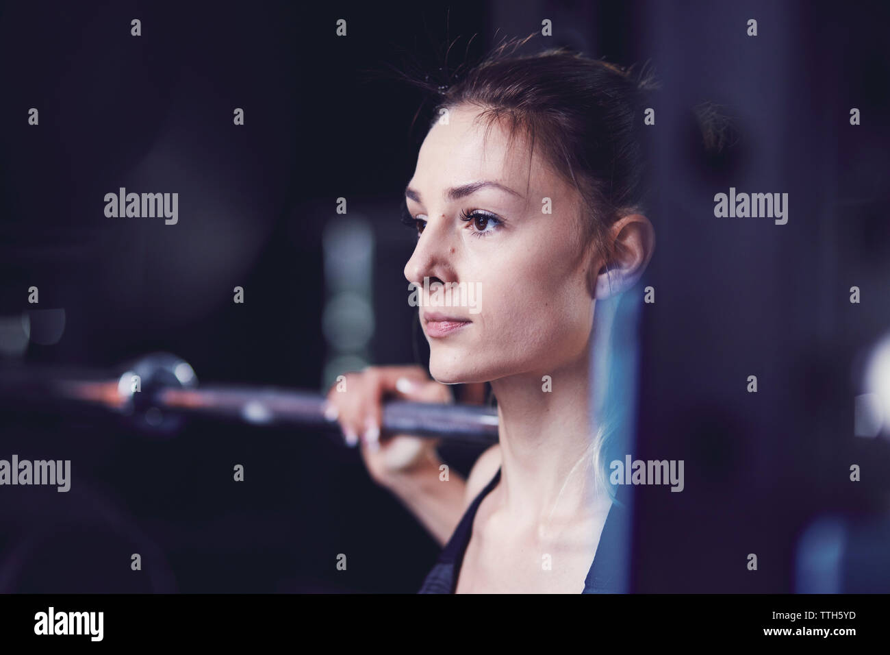 Portrait of young woman looking ahead with barbell at fitness centre Stock Photo