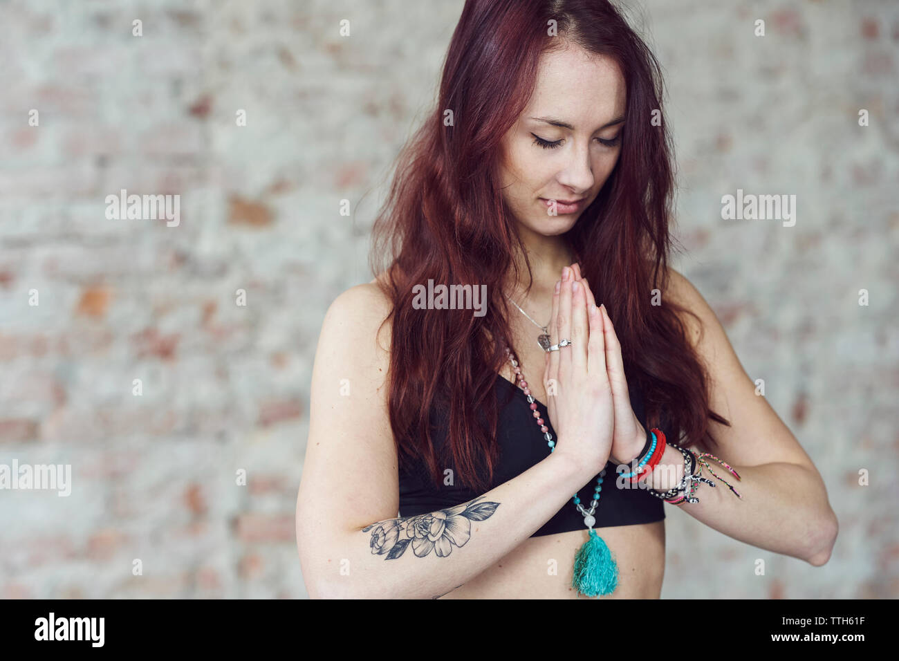Young female in yoga pose with eyes closed by the brick wall Stock Photo