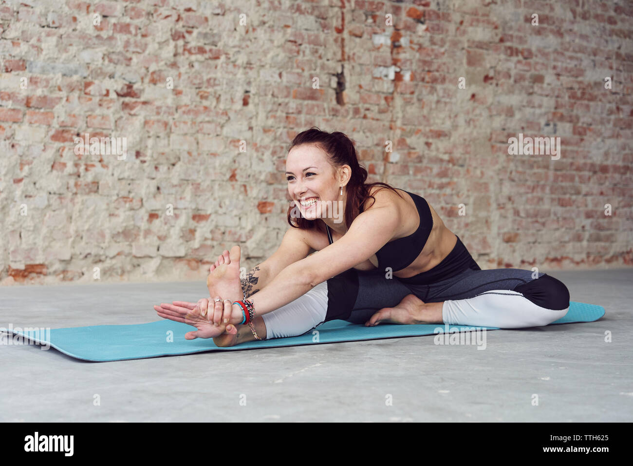 Young female smiling in yoga pose by the brick wall Stock Photo
