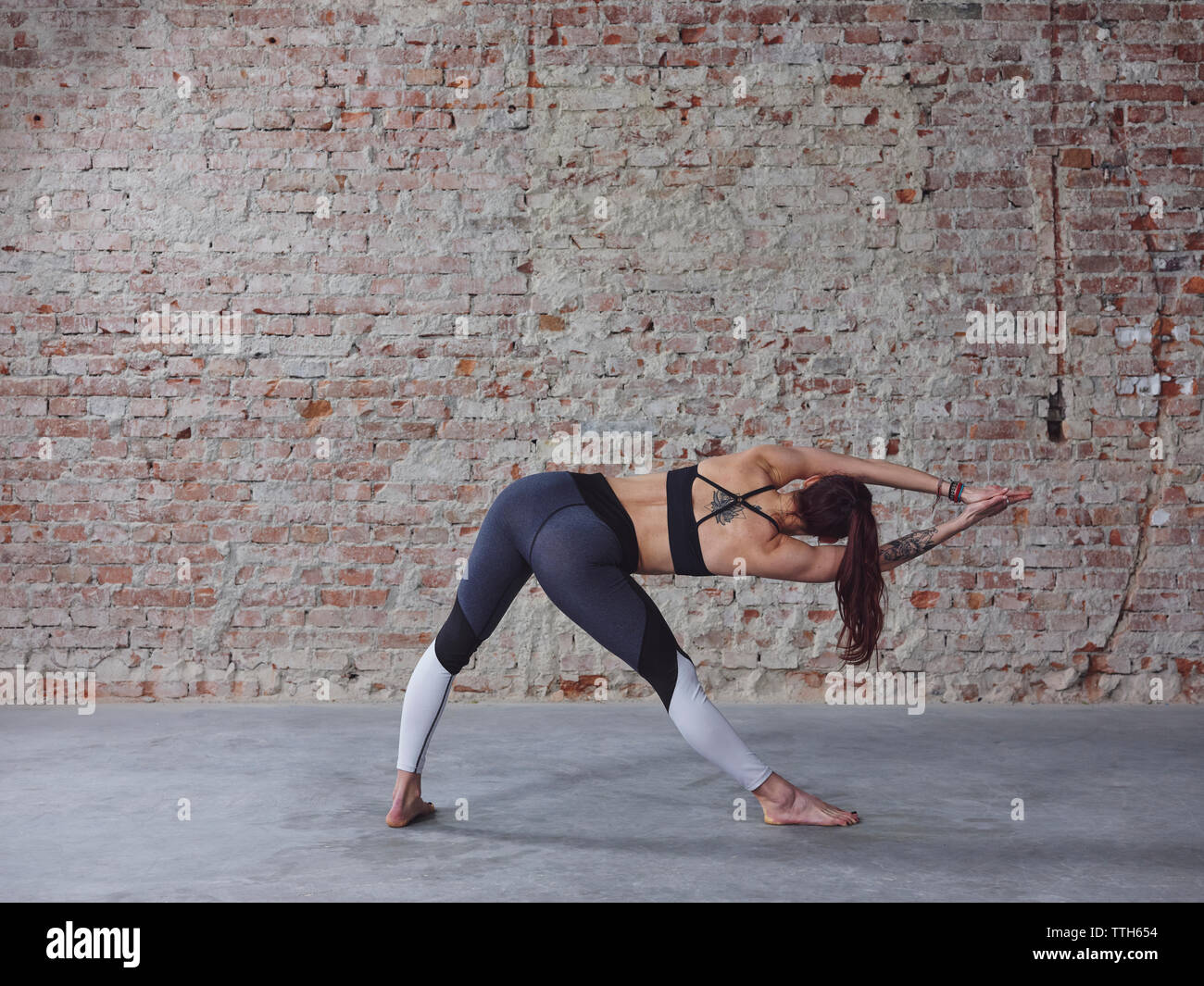Rear profile of young female in yoga pose by the brick wall Stock Photo