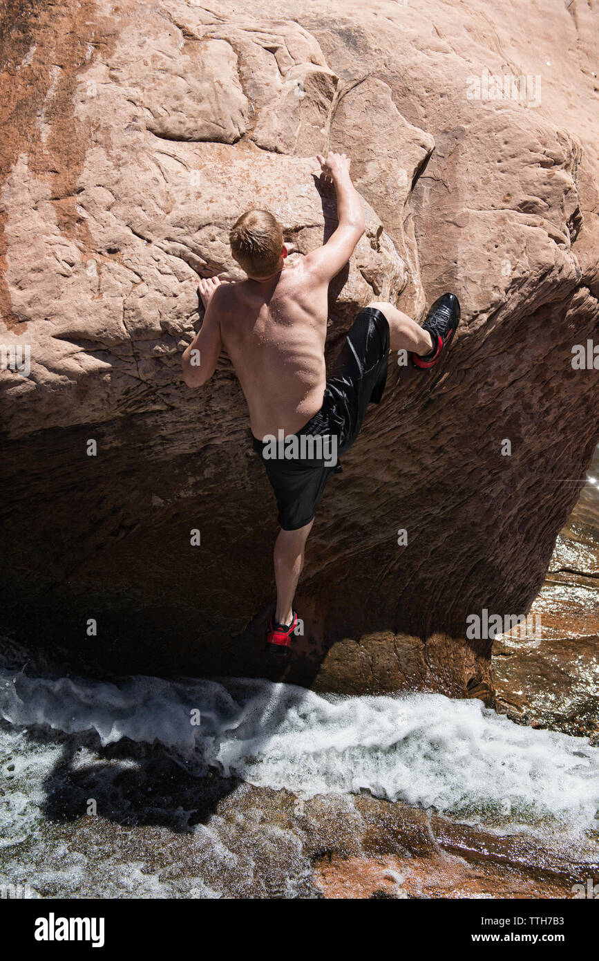 Young man climbs out of backcountry canyon pool in contrasting light Stock Photo