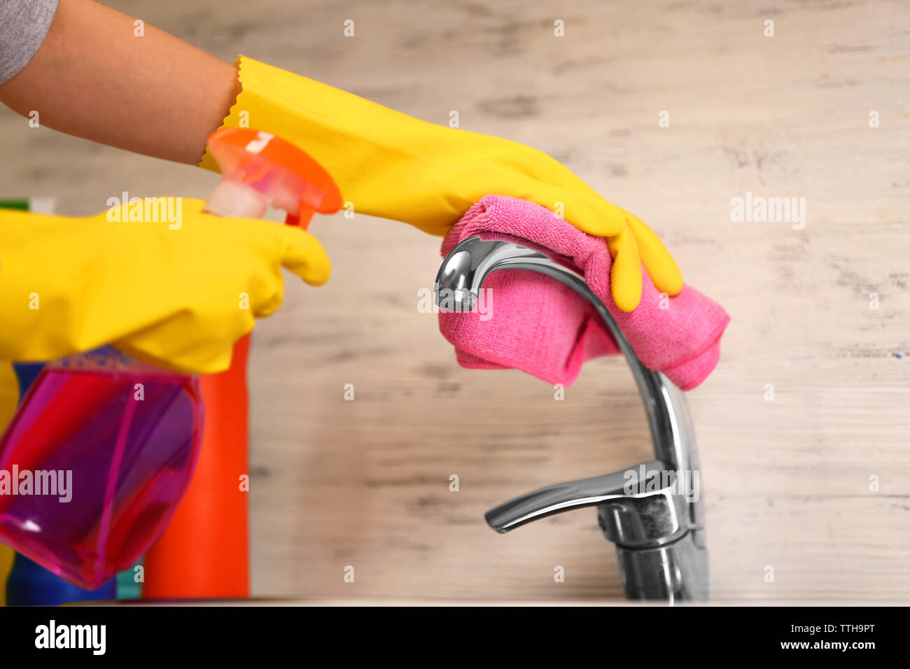 Female hands with rag and detergent spray cleaning a tap in the kitchen ...