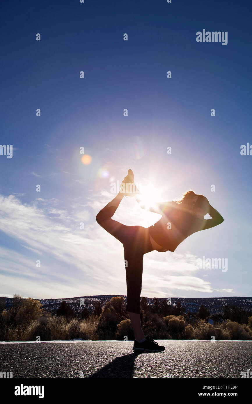 Sporty woman practicing yoga on street against sky during sunny day Stock Photo