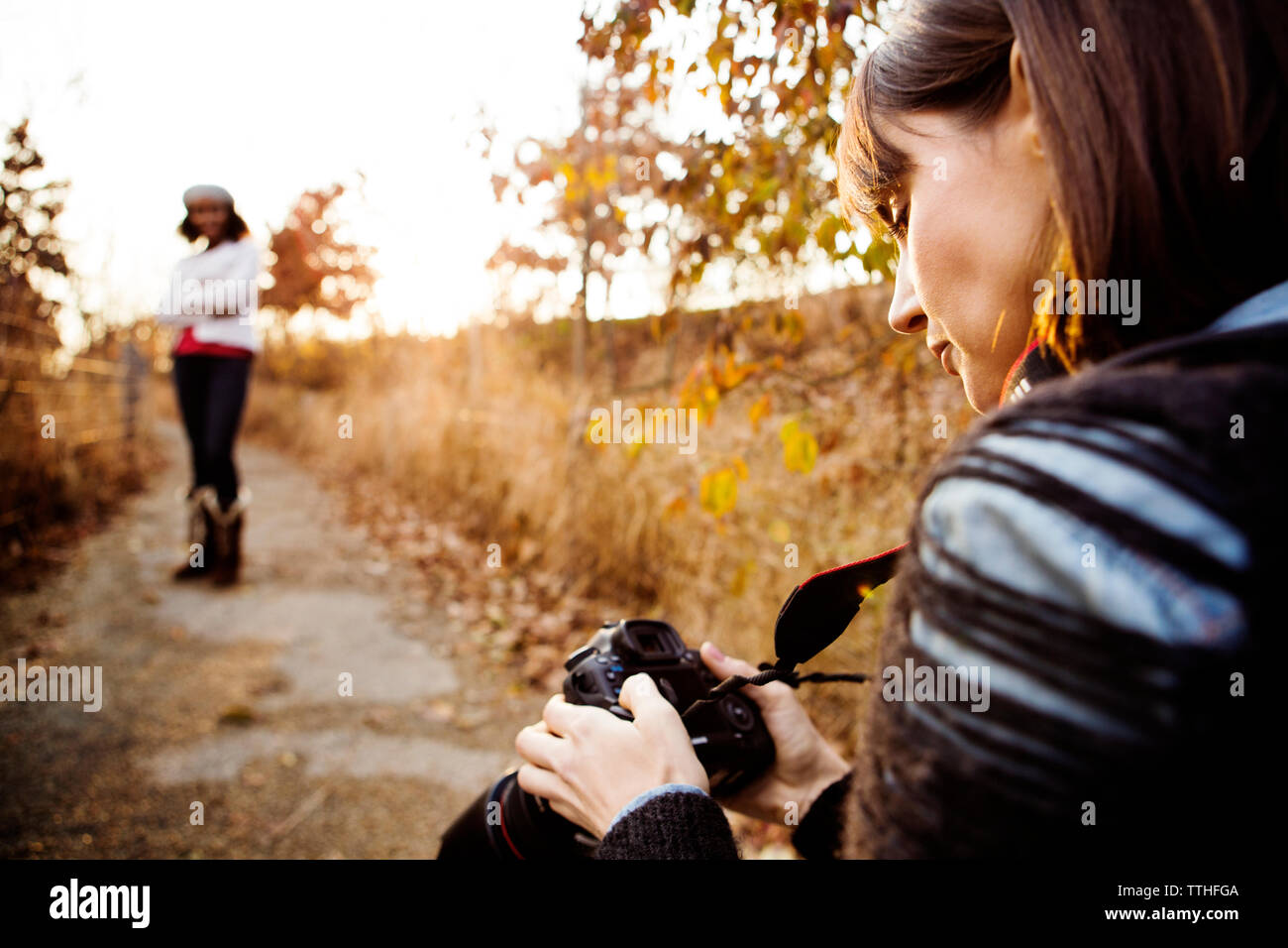 Woman looking at photographs in digital camera while friend posing on footpath Stock Photo