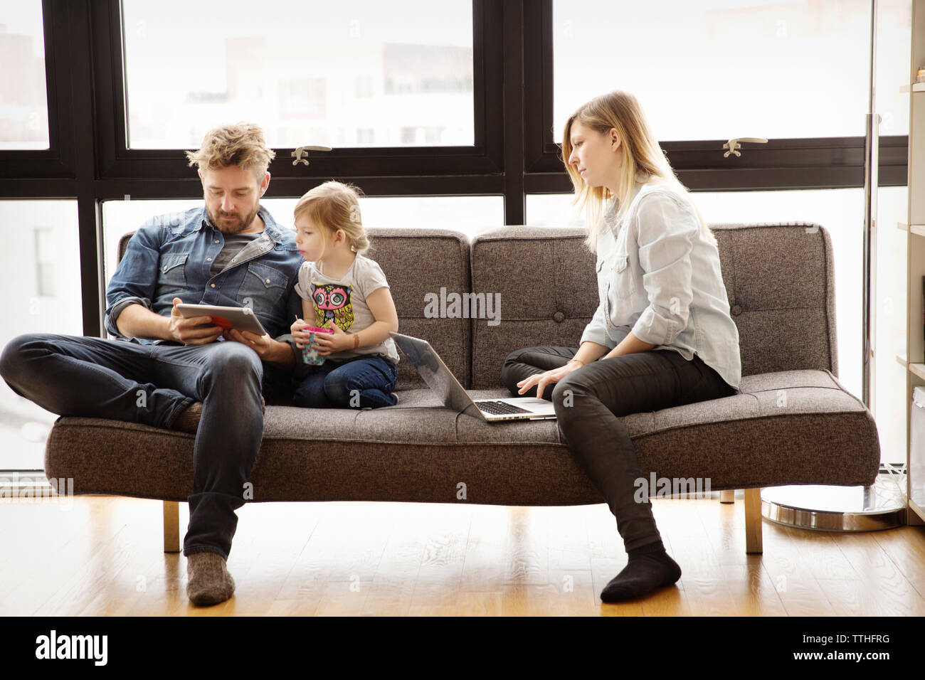 Family using technologies while sitting on sofa at home Stock Photo