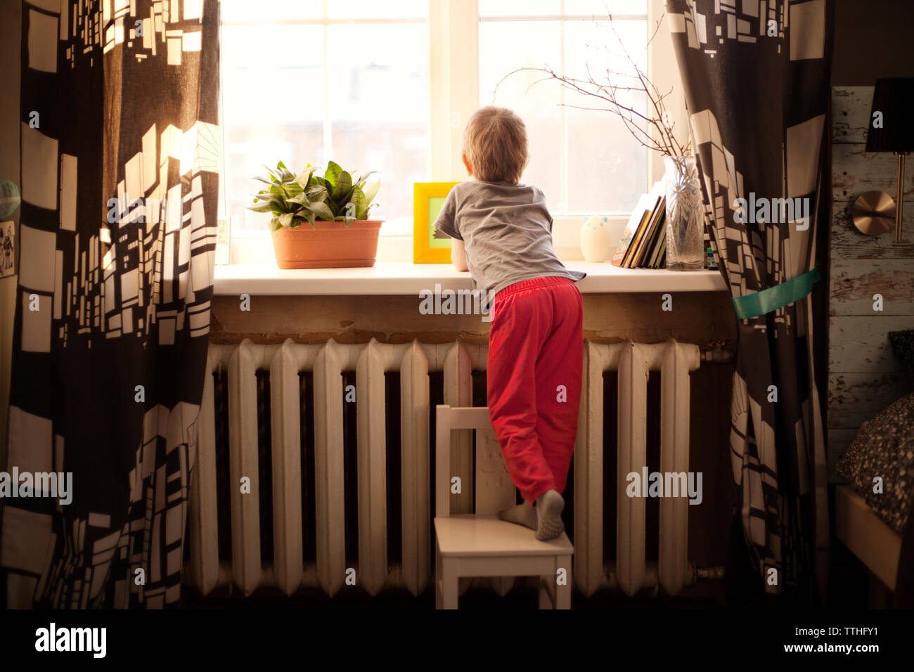 Rear view of boy standing on chair by window at home Stock Photo