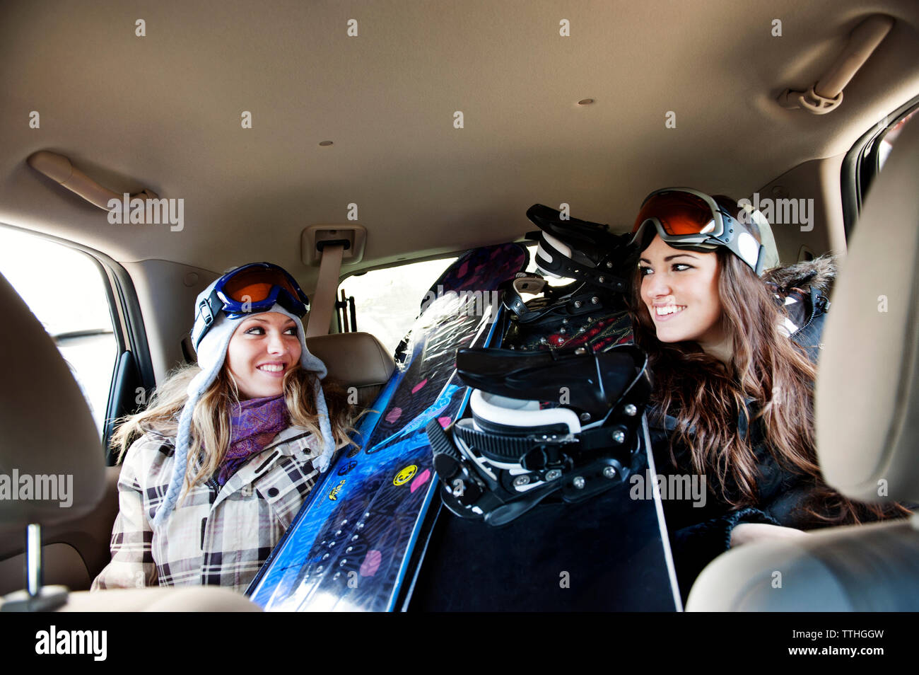 Happy female skiers sitting by snowboards in car Stock Photo