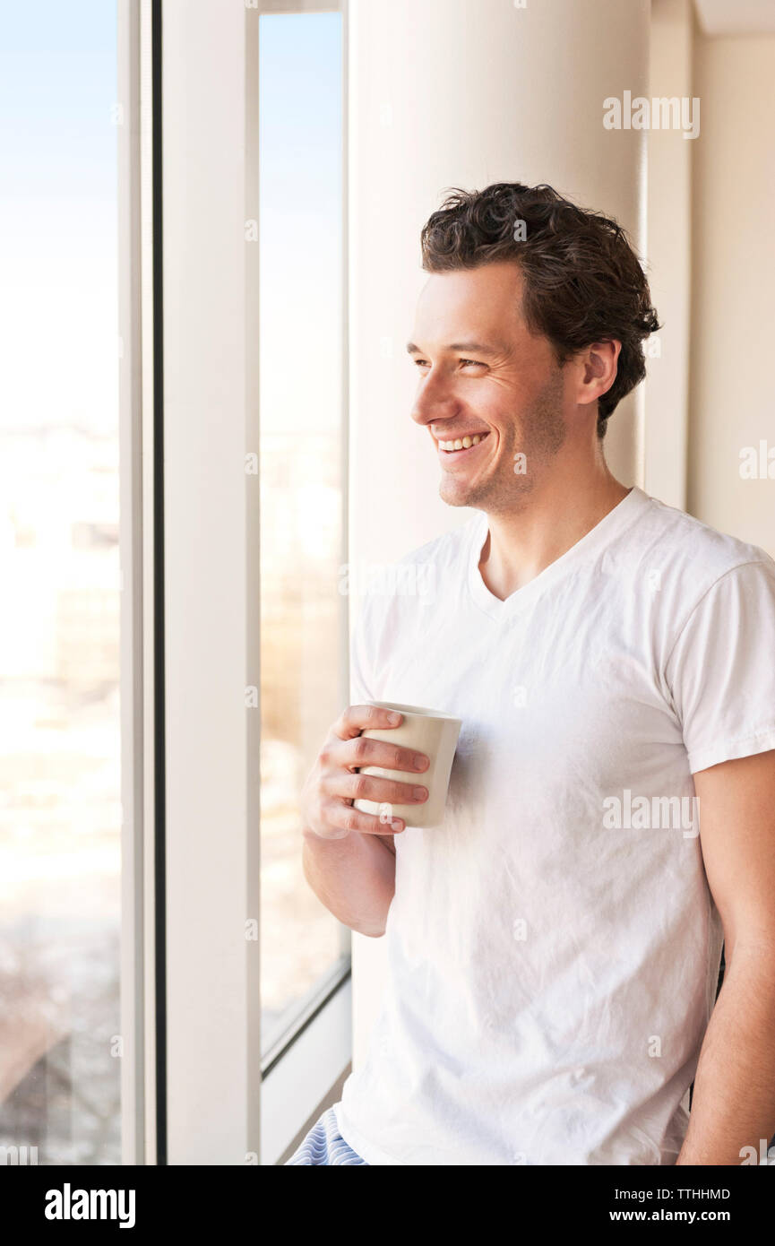 Smiling man drinking coffee and looking though window Stock Photo