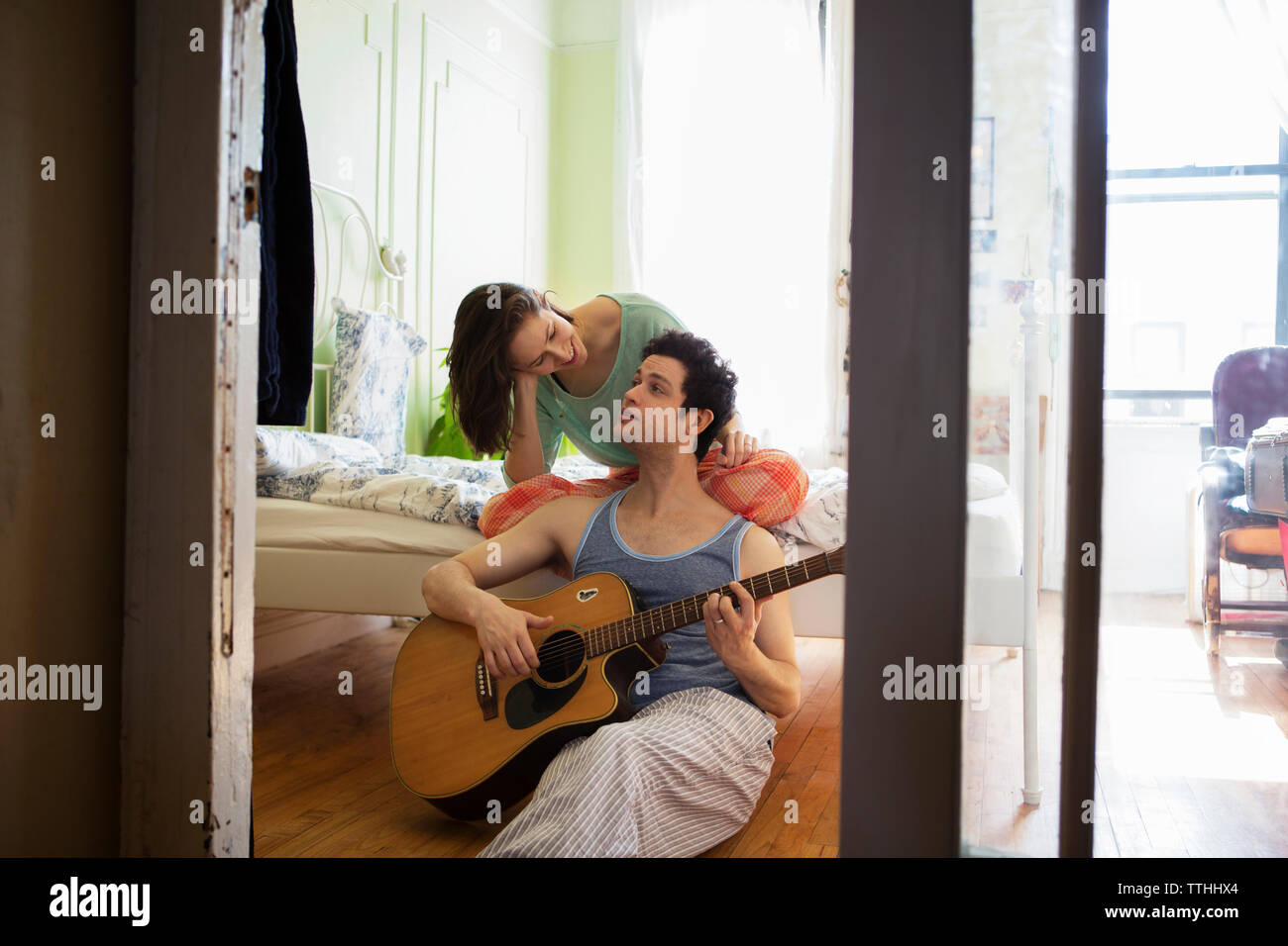 Man playing guitar while looking at girlfriend in bedroom Stock Photo