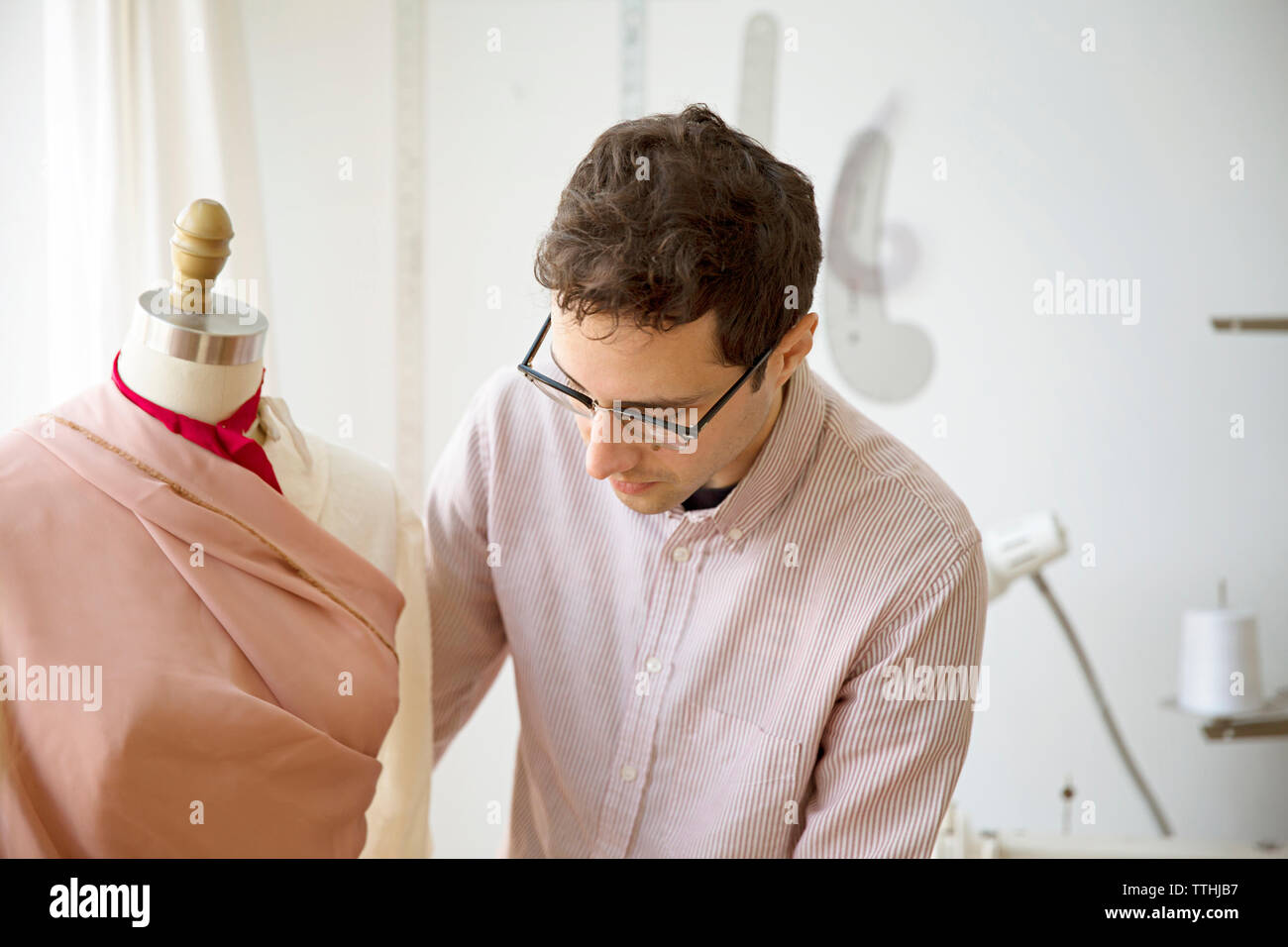 Male fashion designer pinning dress on model at design studio Stock Photo