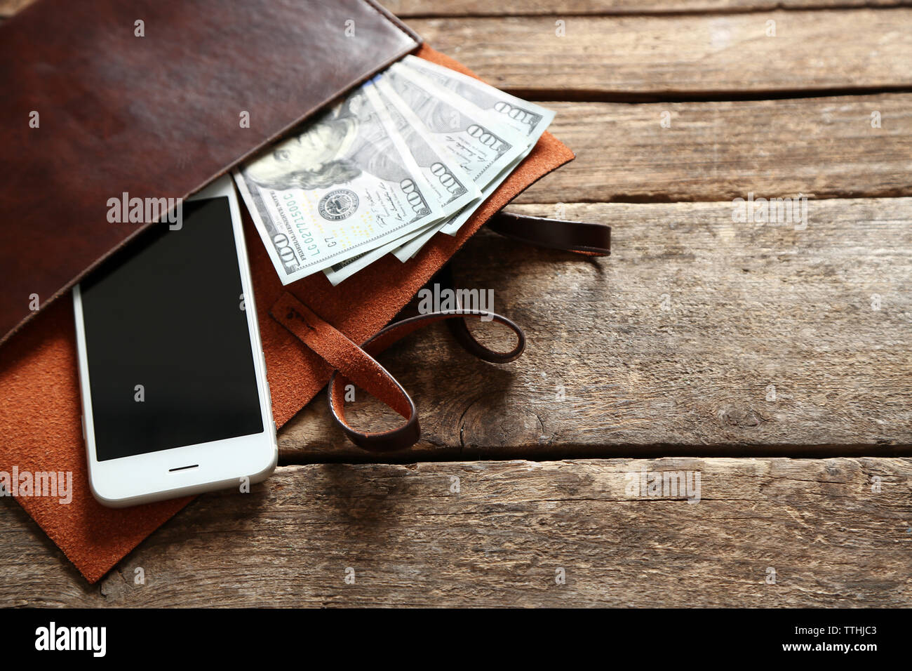 Leather purse with mobile phone and dollar banknotes on wooden table Stock Photo