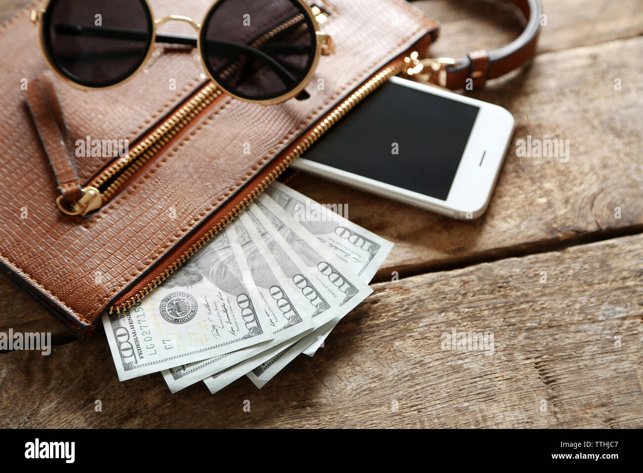 Leather purse with mobile phone, glasses and dollar banknotes on wooden table Stock Photo