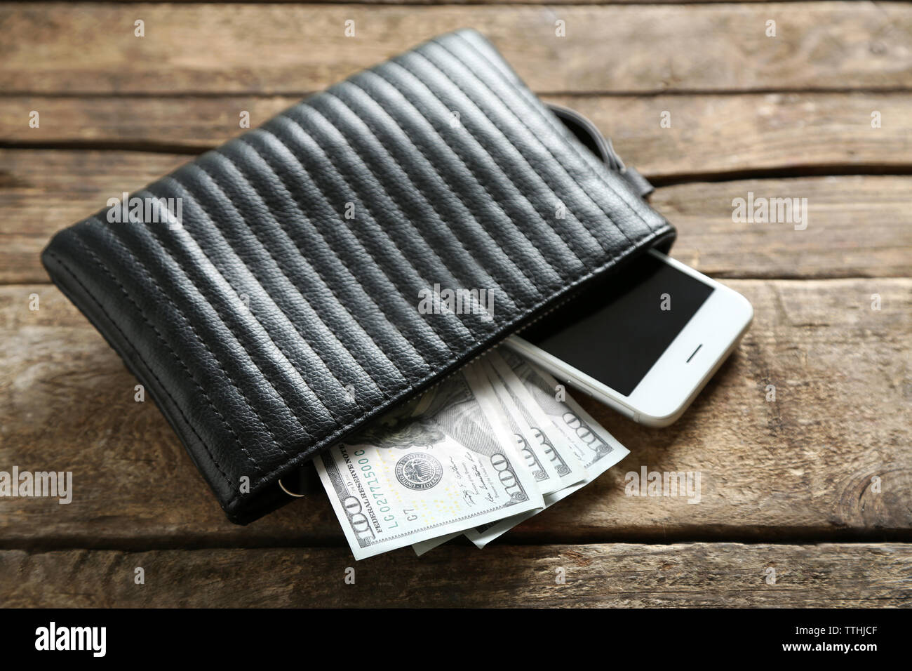 Leather purse with mobile phone and dollar banknotes on wooden table Stock Photo