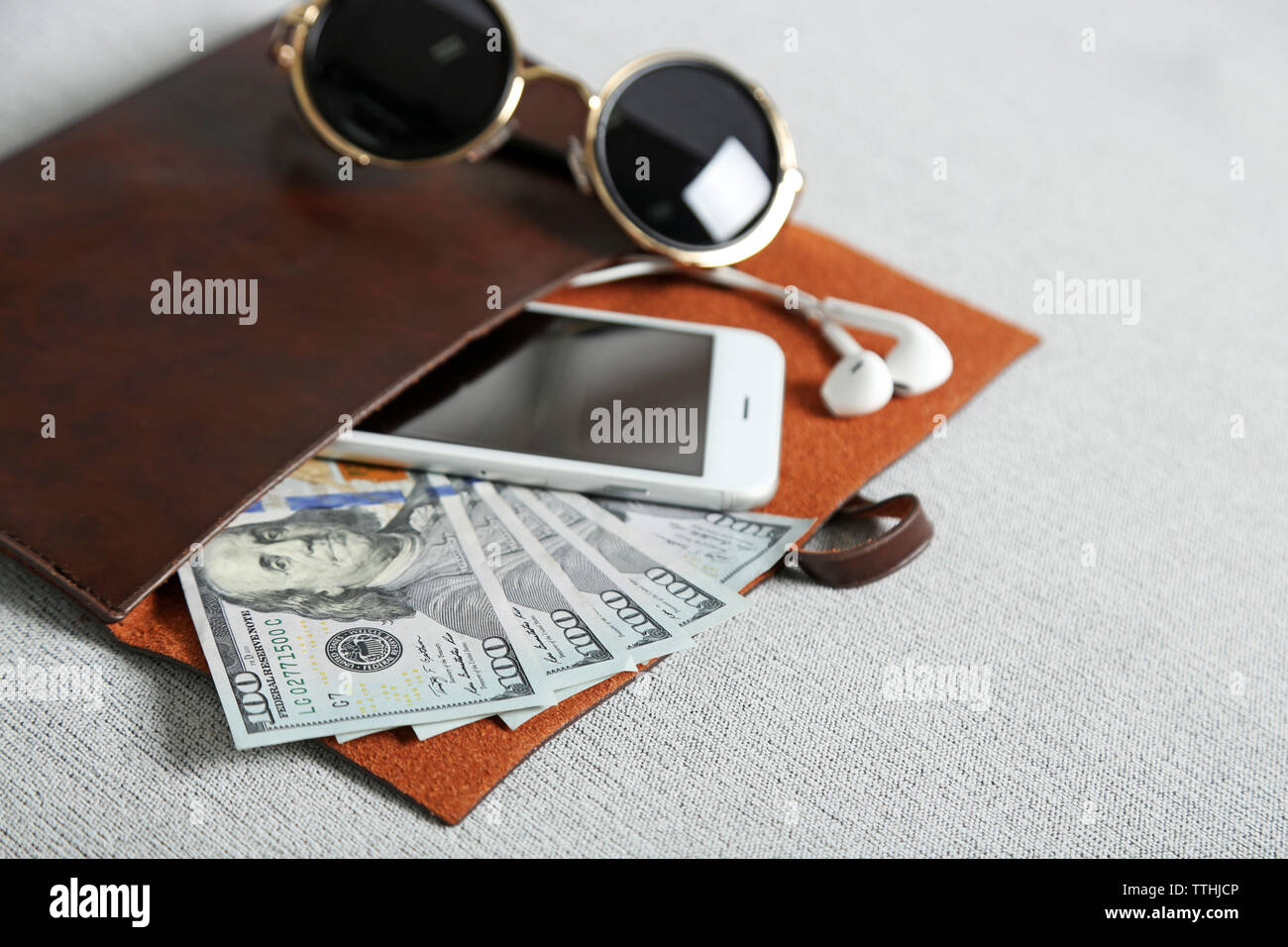 Leather purse with mobile phone, glasses and dollar banknotes on grey cloth background Stock Photo