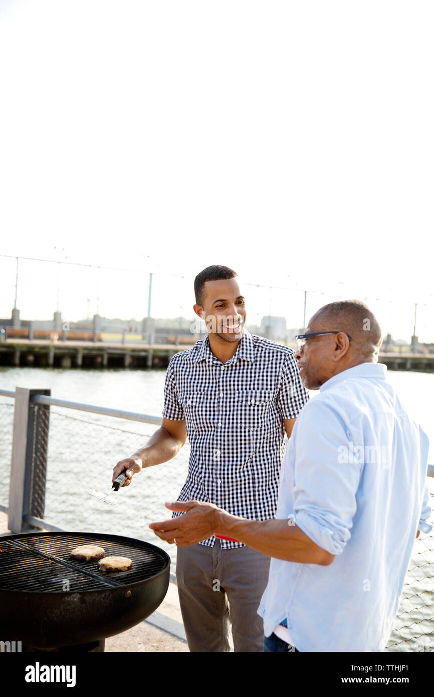 Smiling man preparing food while standing with father by East River against clear sky Stock Photo