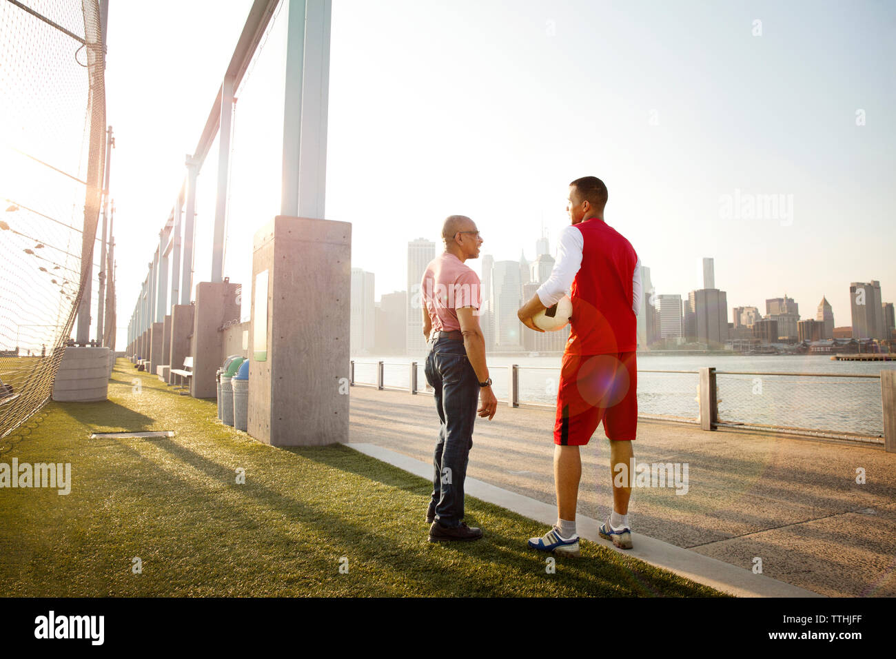 Man holding ball while talking to father at soccer field by East River in city Stock Photo