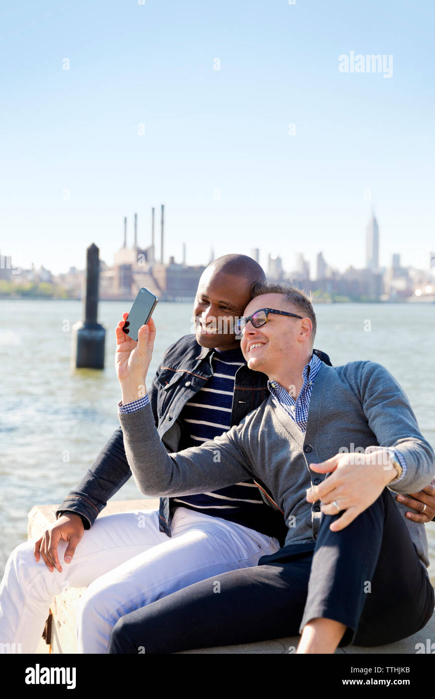 Happy boyfriends taking selfie by river against clear sky on sunny day Stock Photo