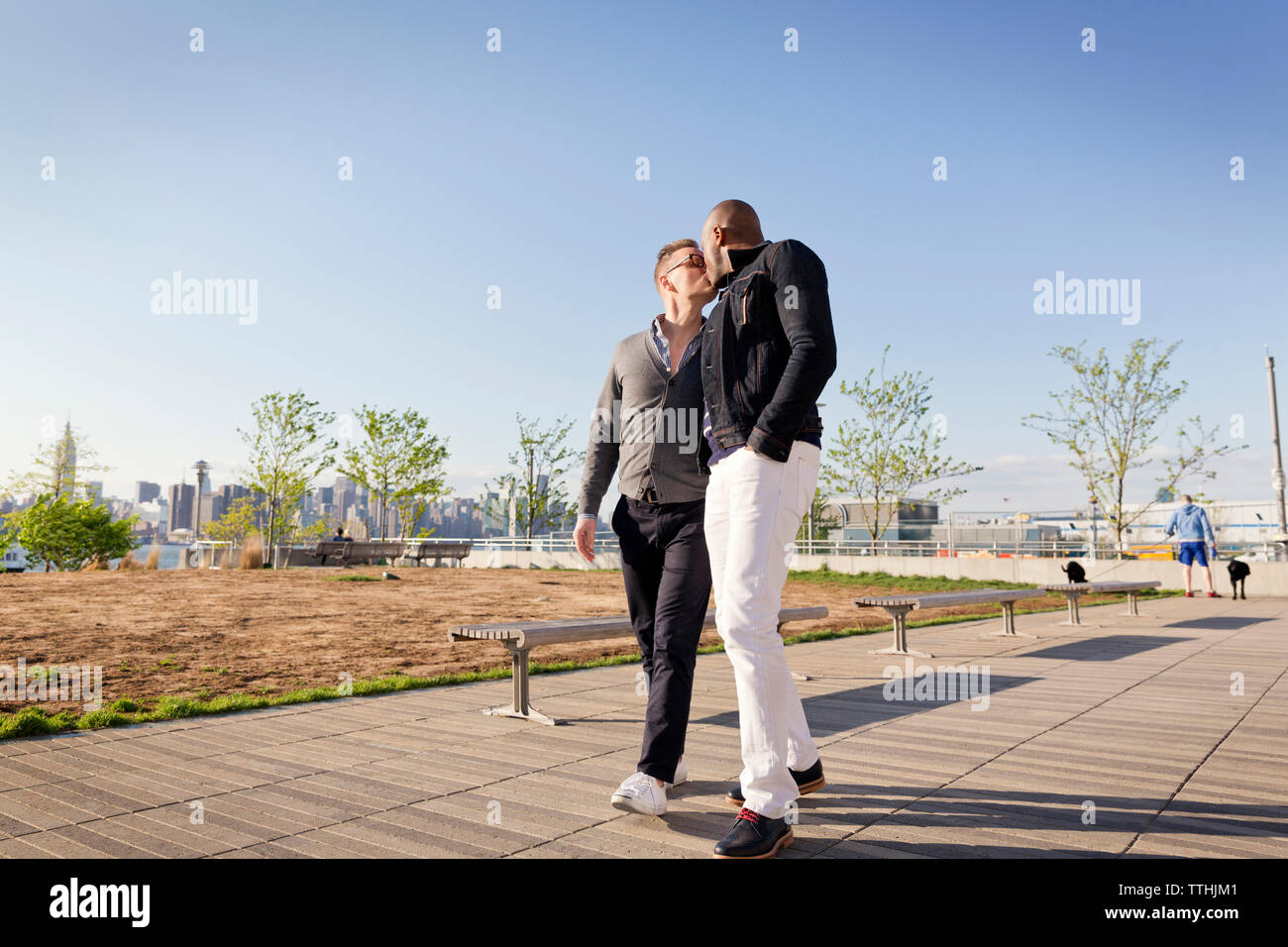 Gay men kissing while walking on footpath in park against clear sky Stock Photo