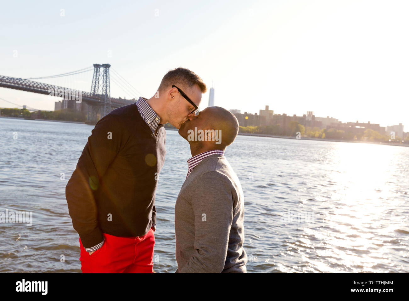 Gay men kissing while standing against East River on sunny day Stock Photo