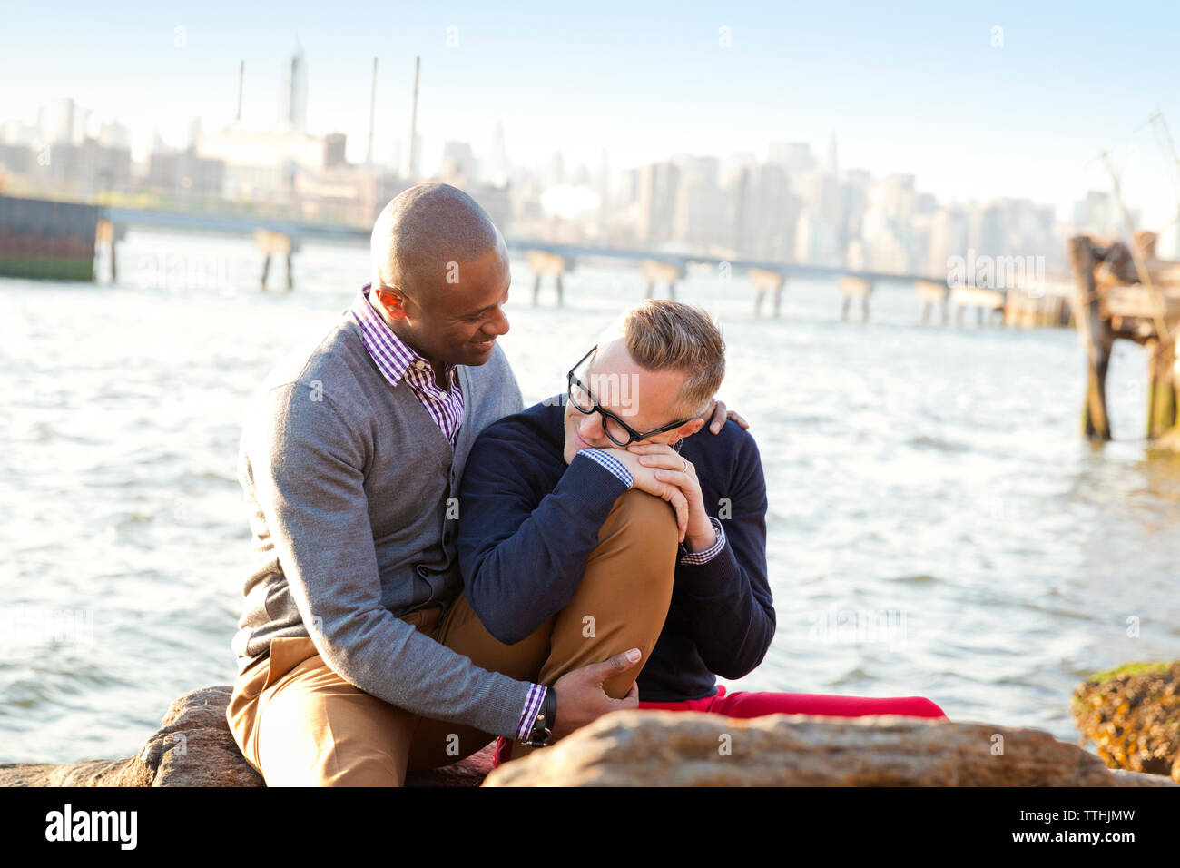 Romantic boyfriends while sitting on rocks against river Stock Photo