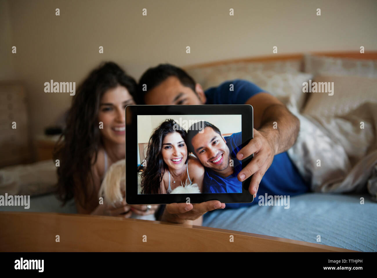 Happy couple taking selfie through tablet computer while relaxing on bed Stock Photo
