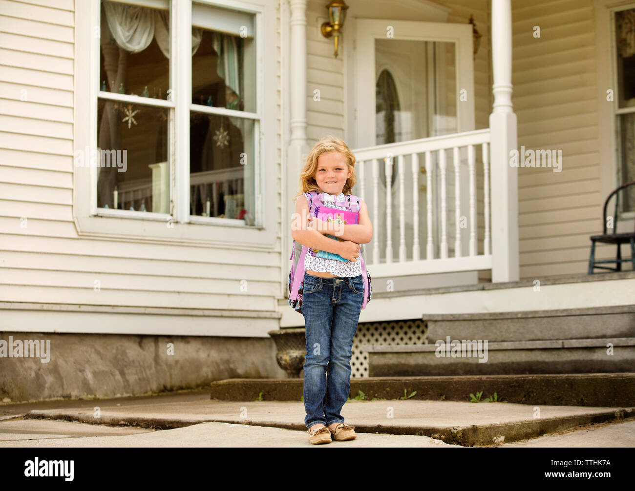 Portrait of happy girl holding books while standing outside house Stock Photo