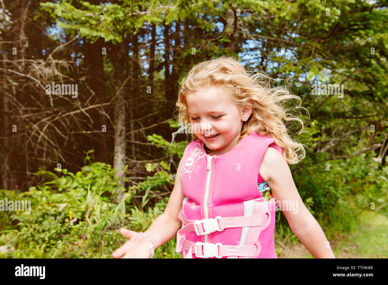 Happy girl wearing life jacket while standing against trees Stock Photo