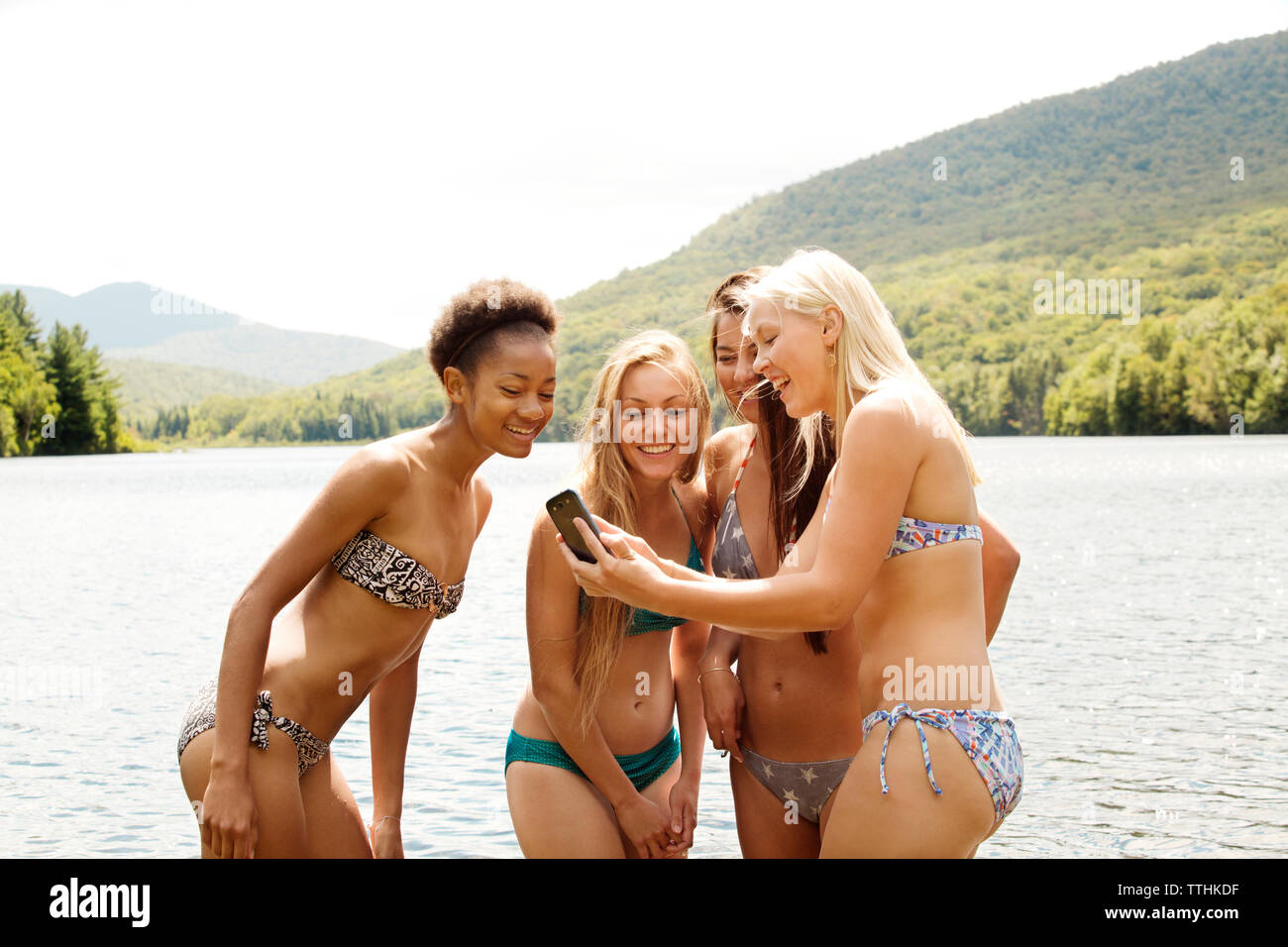 Female friends in bikinis looking at smart phone against lake Stock Photo