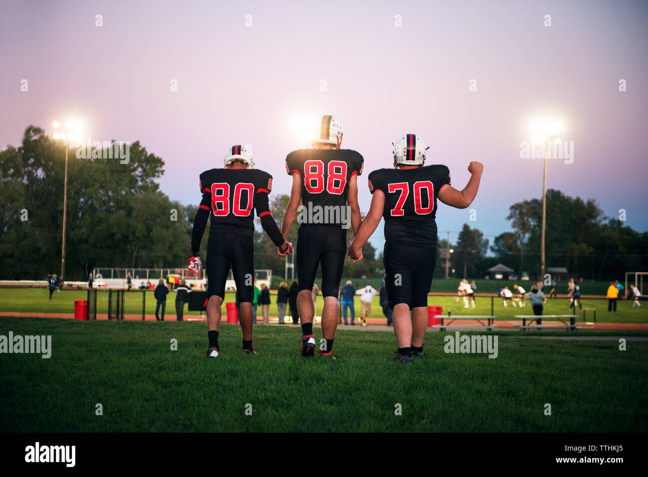 Rear view of American football players holding hands and walking on