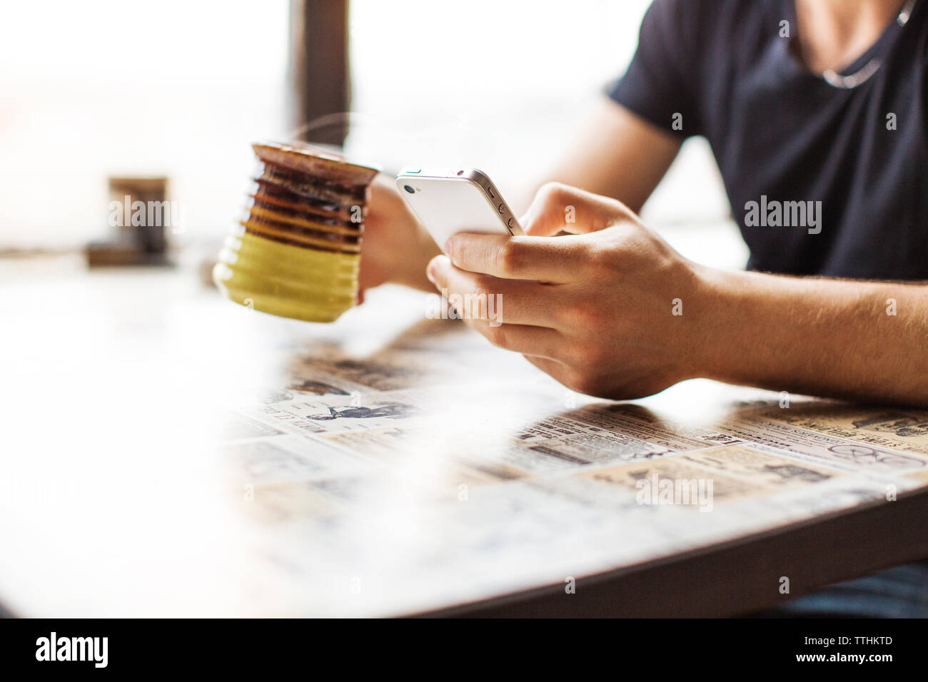 Cropped image of man using smart phone while drinking coffee on table Stock Photo