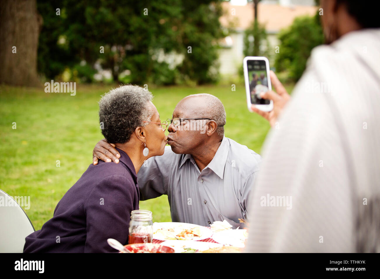 Cropped image of woman photographing senior couple kissing in backyard Stock Photo