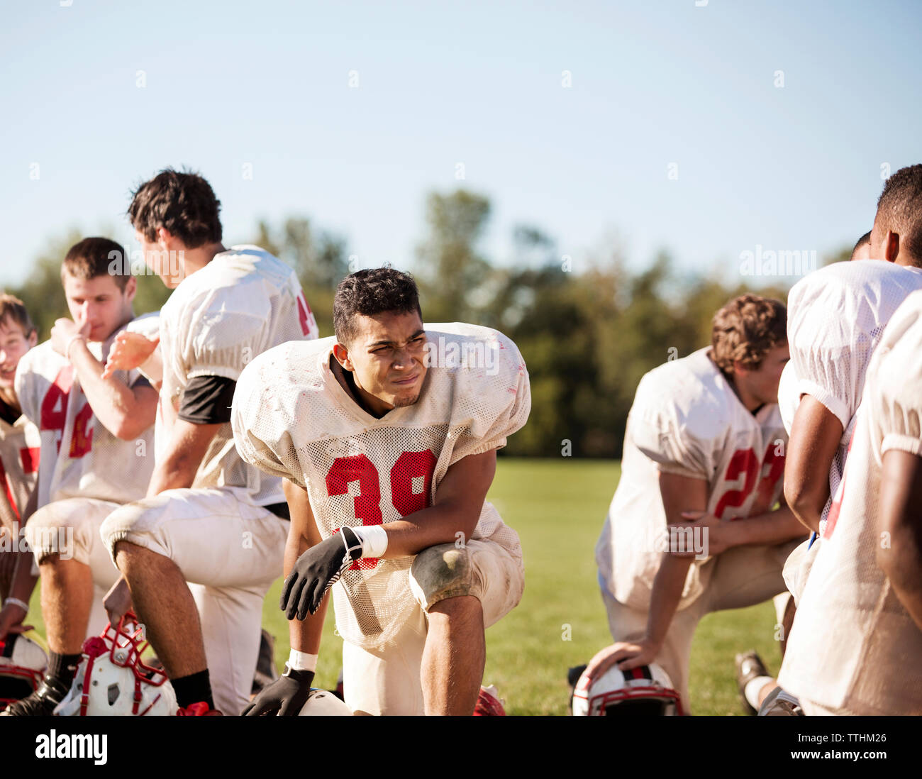 Football players kneeling at playing field on sunny day Stock Photo