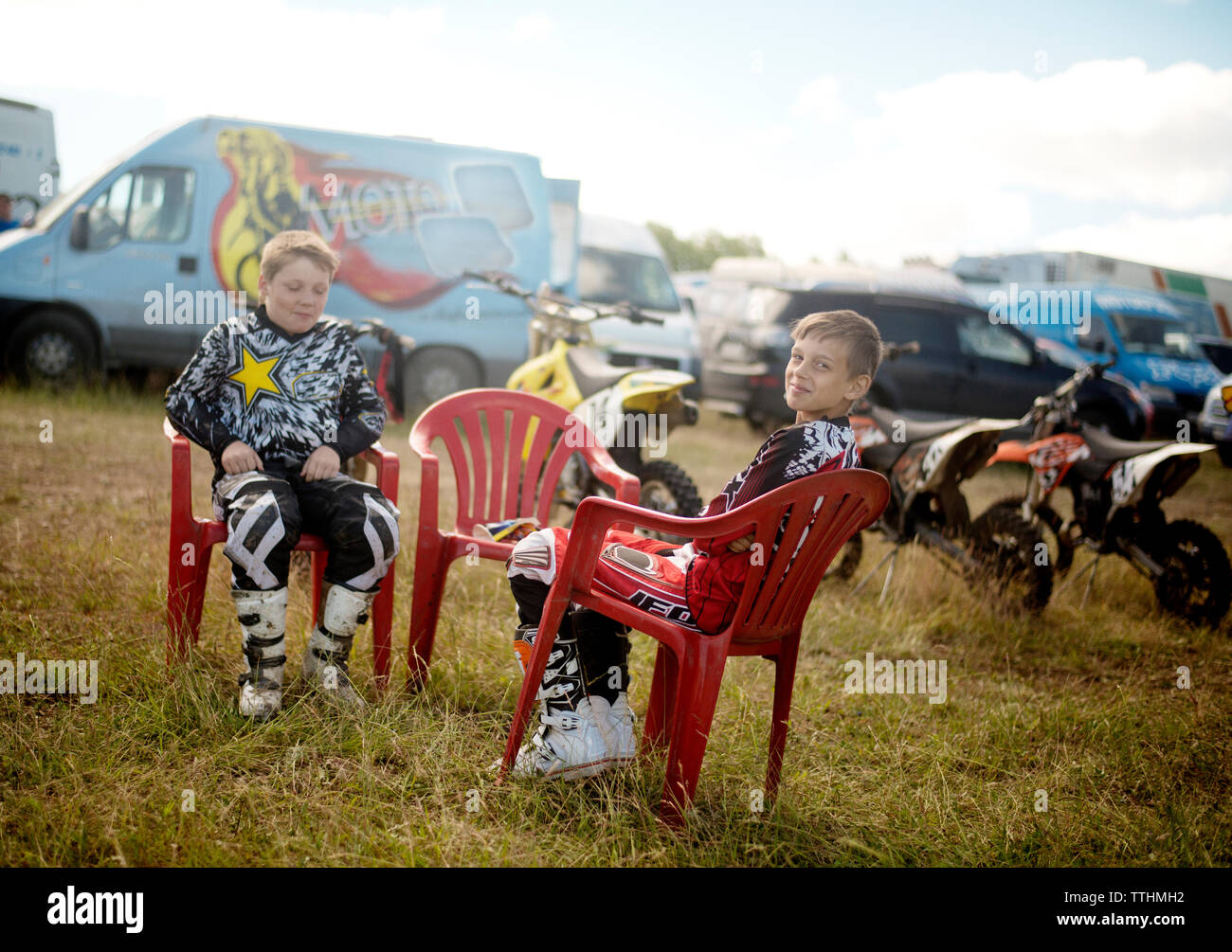 Happy boys sitting on chairs at grassy field Stock Photo